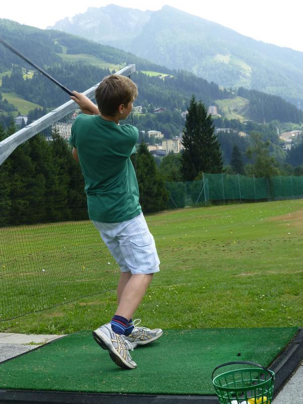 Ein Junge übt im Sommercamp Golf und holt zum Schwung aus