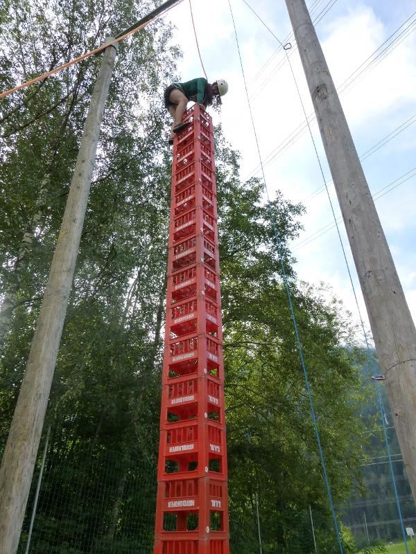 Ein Mädchen klettert im Actioncamp auf einen hohen Turm von roten Kisten