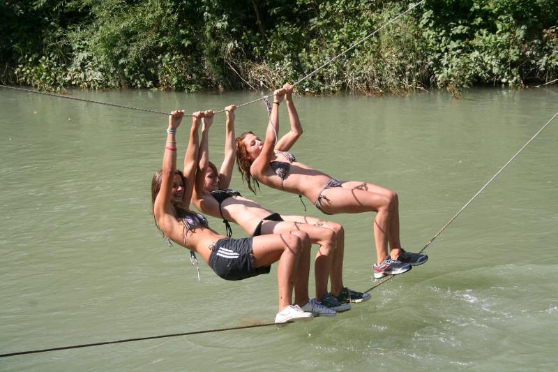 Drei Teilnehmerinnen eines Sommer-Camps balancieren auf einem Seil über einen Fluss