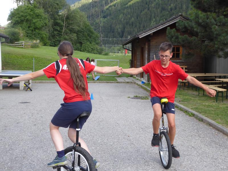 Zwei Teilnehmer üben im Zirkuscamp Einrad fahren im Kreis und halten sich an den Händen fest