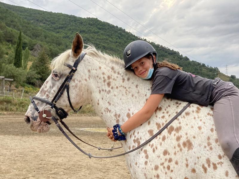 Ein Kind liegt während eines Reitcamps auf dem Rücken eines Pferdes und umarmt den Hals des Pferdes