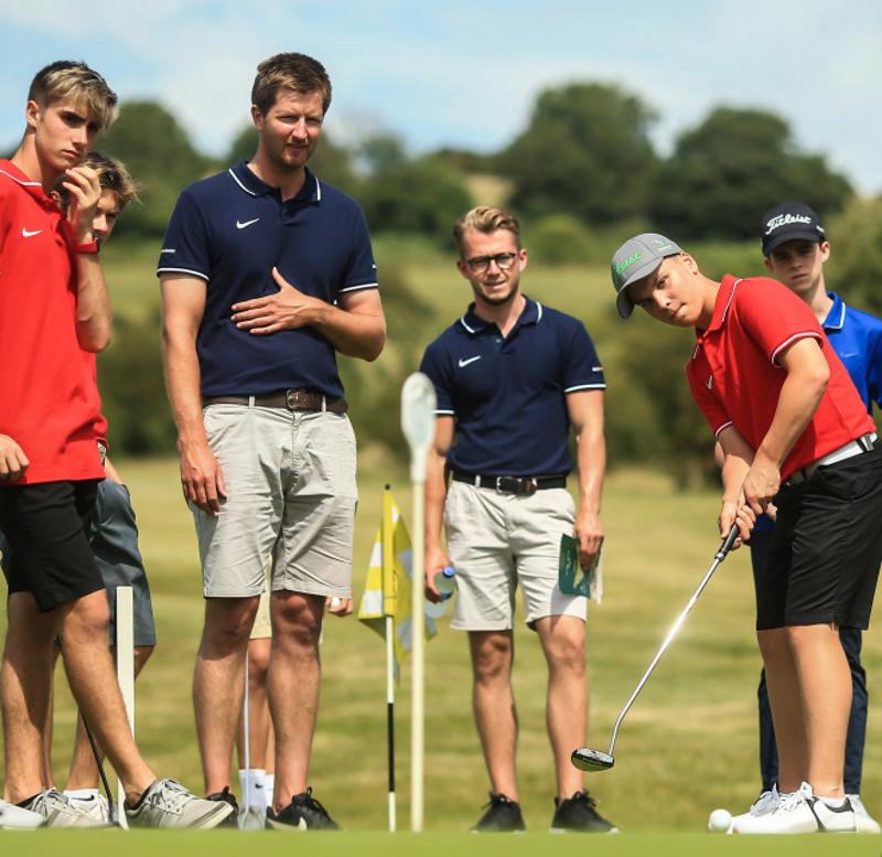 Mehrere Trainer und Teilnehmer des Golf-Camps Österreich schauen zu wie jemand der Golfball schlägt