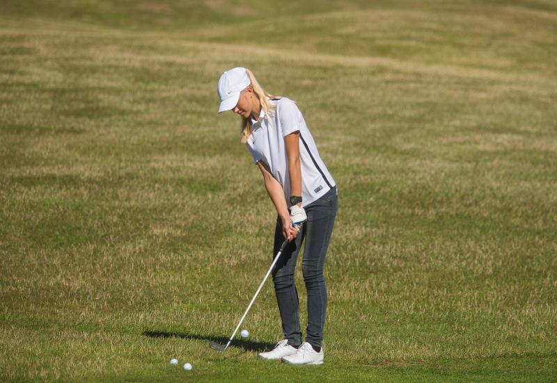 Teilnehmerin eines Golfcamps trägt weiße Kleidung und übt den Golfschlag