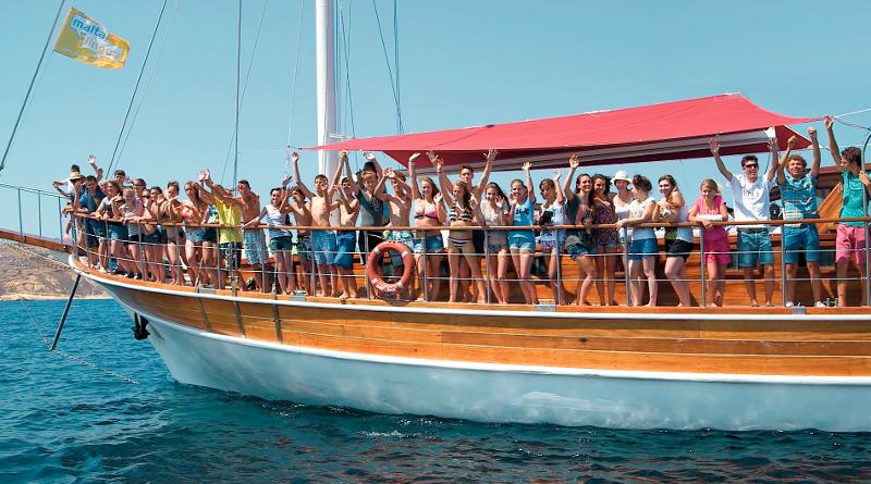 Die Teilnehmer der Sprachreise Malta stehen auf einem Boot und heben die Hände in die Luft