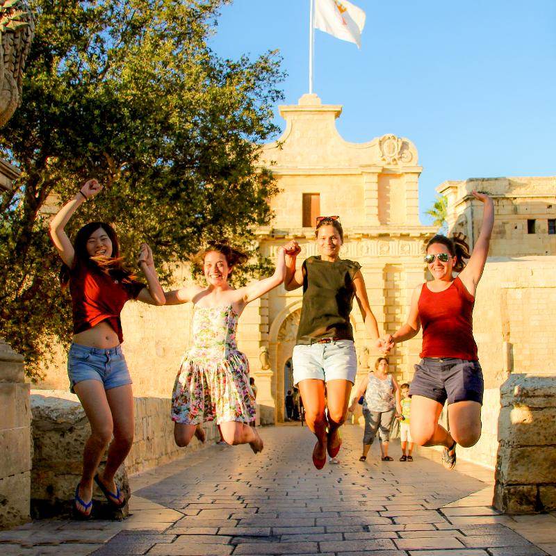 Vier Freunde springen auf Sprachreise Malta vor einer Burg in die Luft