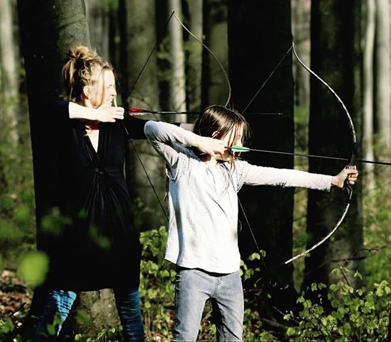 Zwei Mädchen üben Bogenschießen im grünen Wald in der Ferienbetreuung Wien