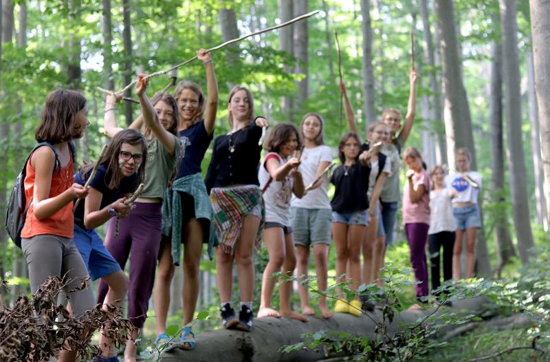Eine Gruppe Mädchen steht mit erhobenen Stöcken im Wald