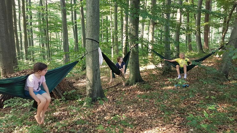 Drei Mädchen sitzen auf Hängematten zwischen Bäumen im Wald
