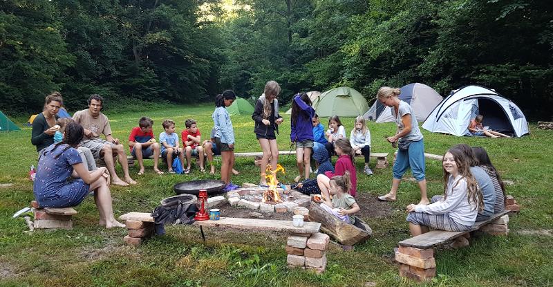 Kinder sitzen im Wald auf einer Lichtung um eine Lagerfeuer