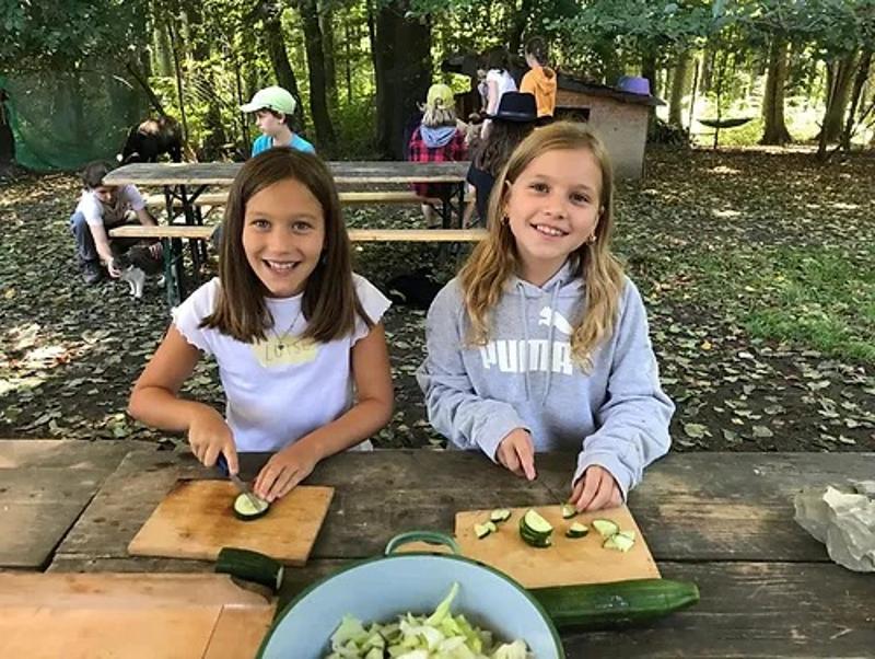 Zwei Mädchen schneiden Gemüse auf Holzbrettchen in kleine Stücke während einem Feriencamp Mödling