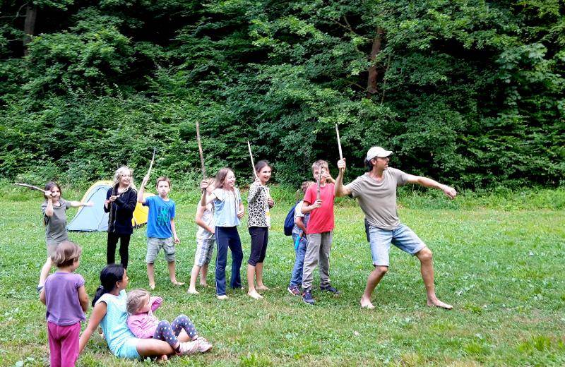 Im Summercamp spielen stehen die Kinder in einer Reihe und halten Stöcker aus Holz in den Händen