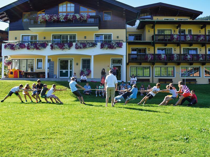 In der Ferienbetreuung Innsbruck treten die Teilnehmer im Tauziehen gegeneinander an vor der Unterkunft