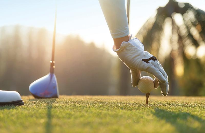 Eine Hand die einen Handschuh trägt legt einen Golfball auf einen Tee
