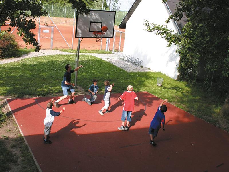 Kindergruppe spielt mit ihrem Betreuer eine Runde Basketball auf einem Sportplatz