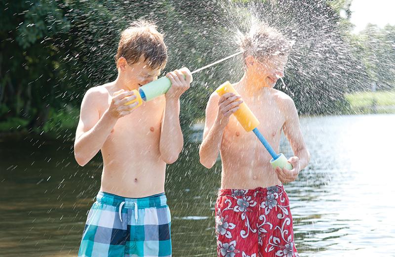Zwei Teilnehmer eines Sommersportcamps besprühen sich mit Wasser aus ihren Spritzpistolen