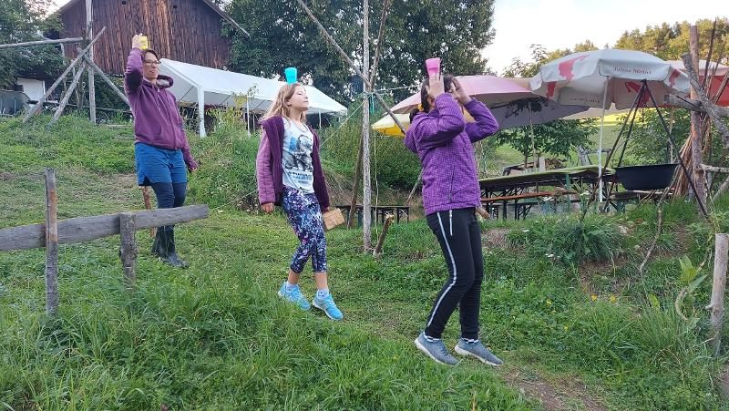 Die Teilnehmer des Familiencamps balancieren mit Wasser gefüllte Becher auf ihren Köpfen